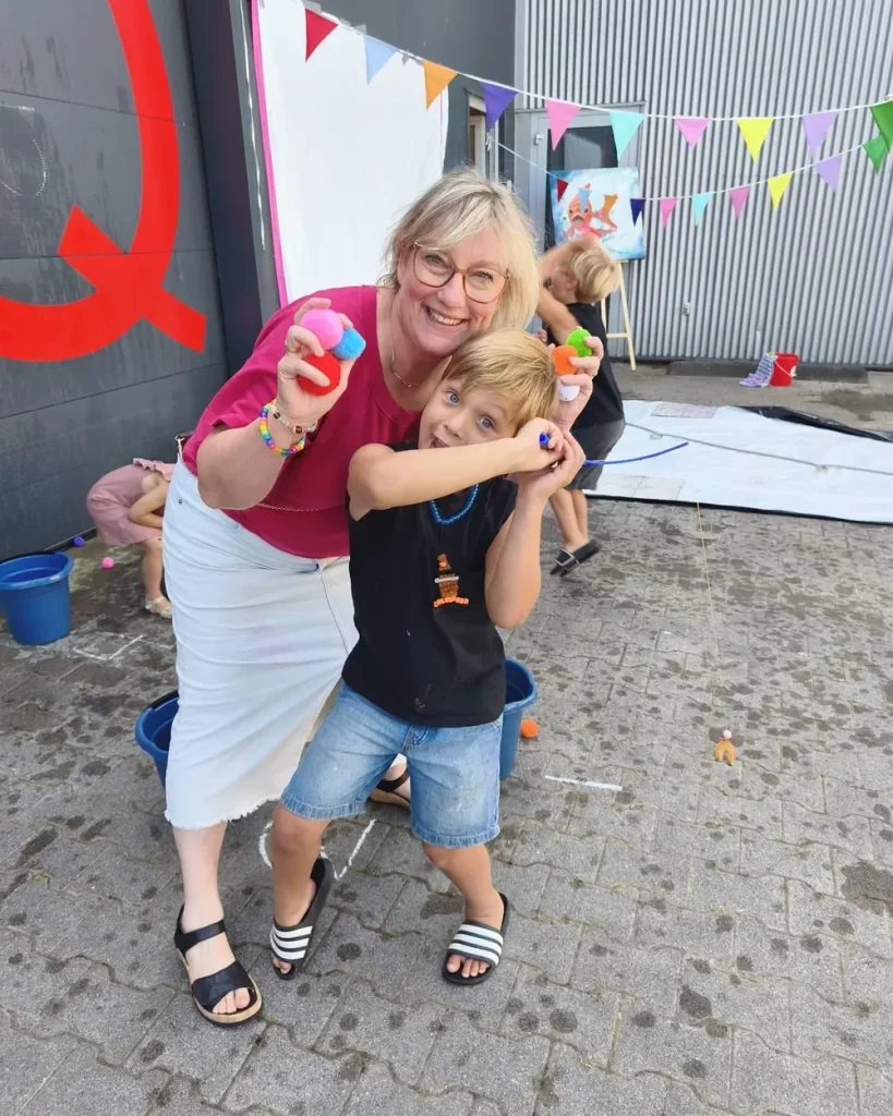 Ine van Mil lacht met een jongen tijdens een kinderfeestje, met pompons in de hand